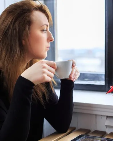 Femeie care bea cafea la fereastră, privind afară
