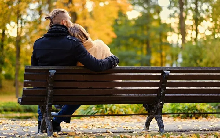 Un cuplu văzut din spate, pe o bancă într-un parc, toamna